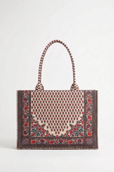 A structured tote bag with a woven pattern featuring a central beige and brown geometric motif, red floral accents, and a dark brown border, complete with braided shoulder straps, shown against a plain light gray background.