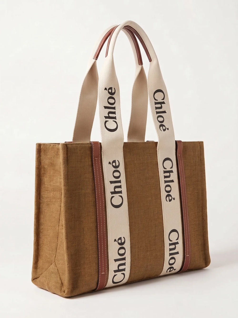 A brown canvas tote bag with cream-colored shoulder straps featuring the black 'Chloé' logo printed repeatedly, set against a plain off-white background.