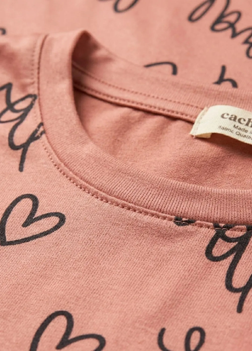 Close-up of a pink shirt with black text and a visible brand label.