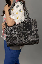 Person holding a black and white patterned tote bag against a gray background