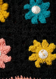 Close up of a black fabric with colorful knitted flowers.