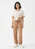 Woman wearing a cream t-shirt with a bear design and beige pants with bear prints on a white background
