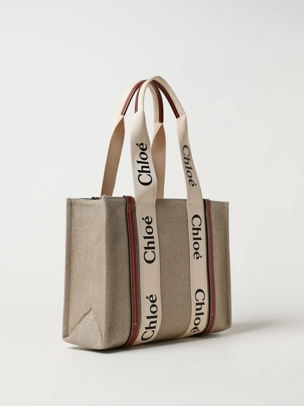 A gray canvas tote bag with cream-colored shoulder straps featuring the black 'Chloé' logo, accented by thin red stripes along the sides, shown on a light gray background.