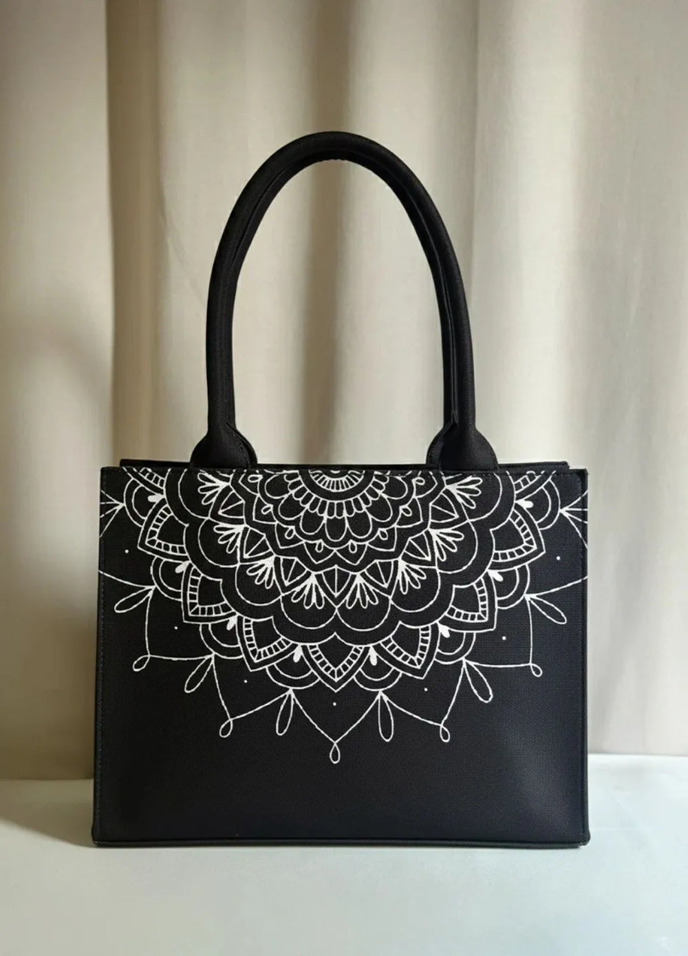 Black women handbag with white mandala design on a beige curtain background