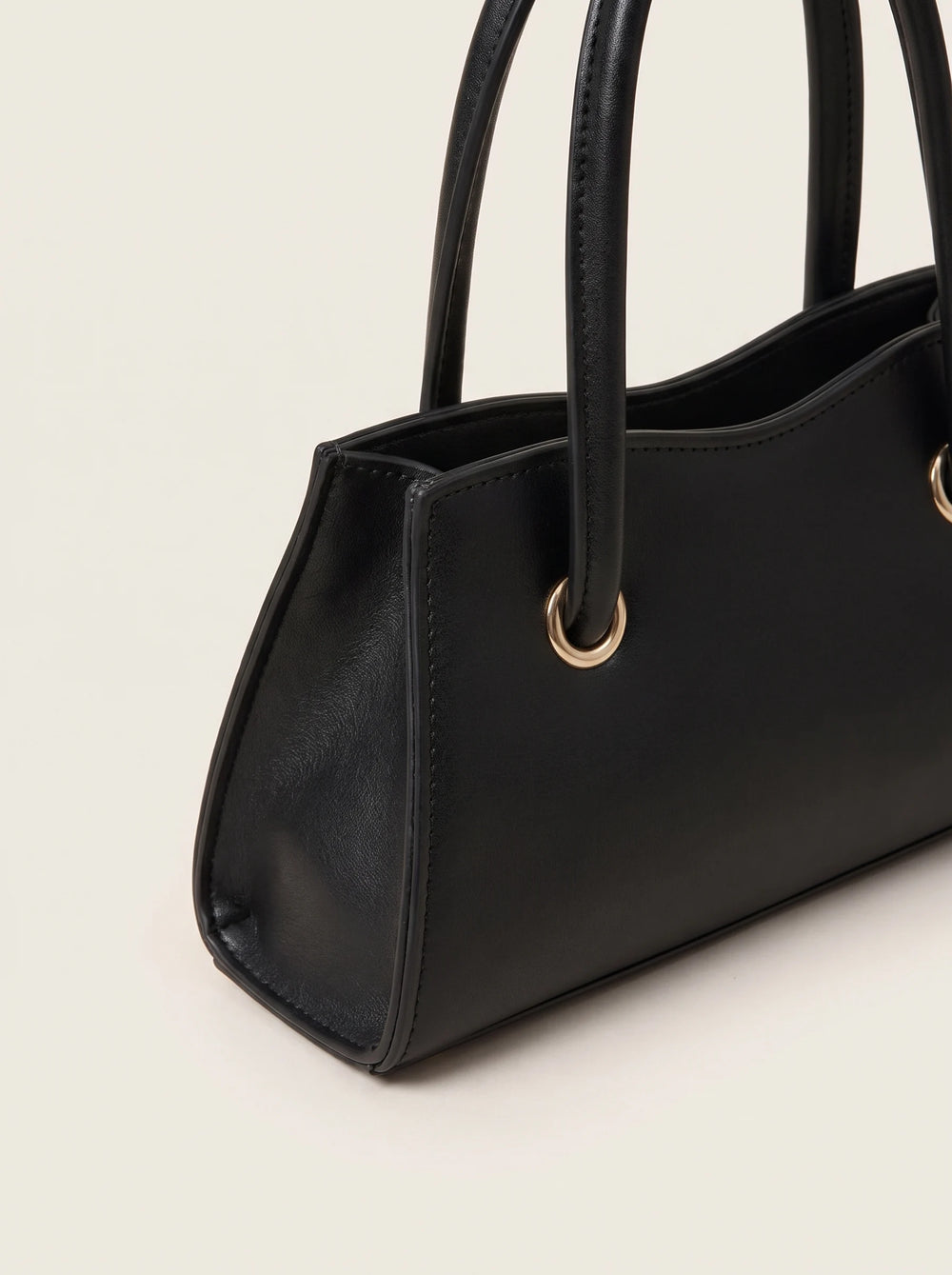A close-up of a black leather handbag with double top handles and gold-tone metal hardware, set against a plain off-white background.