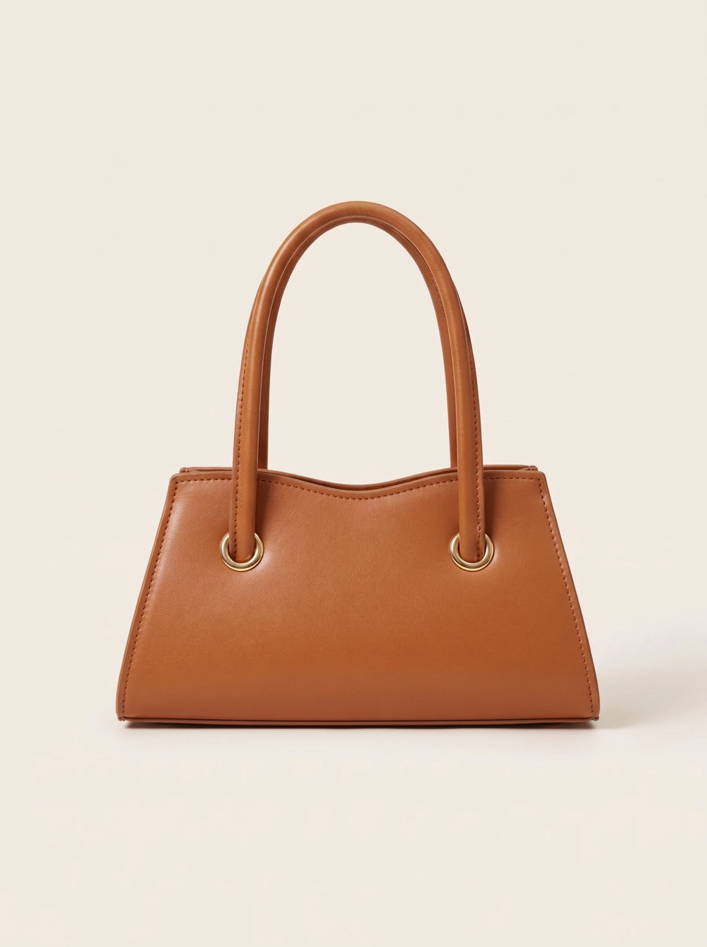 A tan pu leather handbag with double top handles and gold-tone metal grommets, photographed against a solid off-white background.