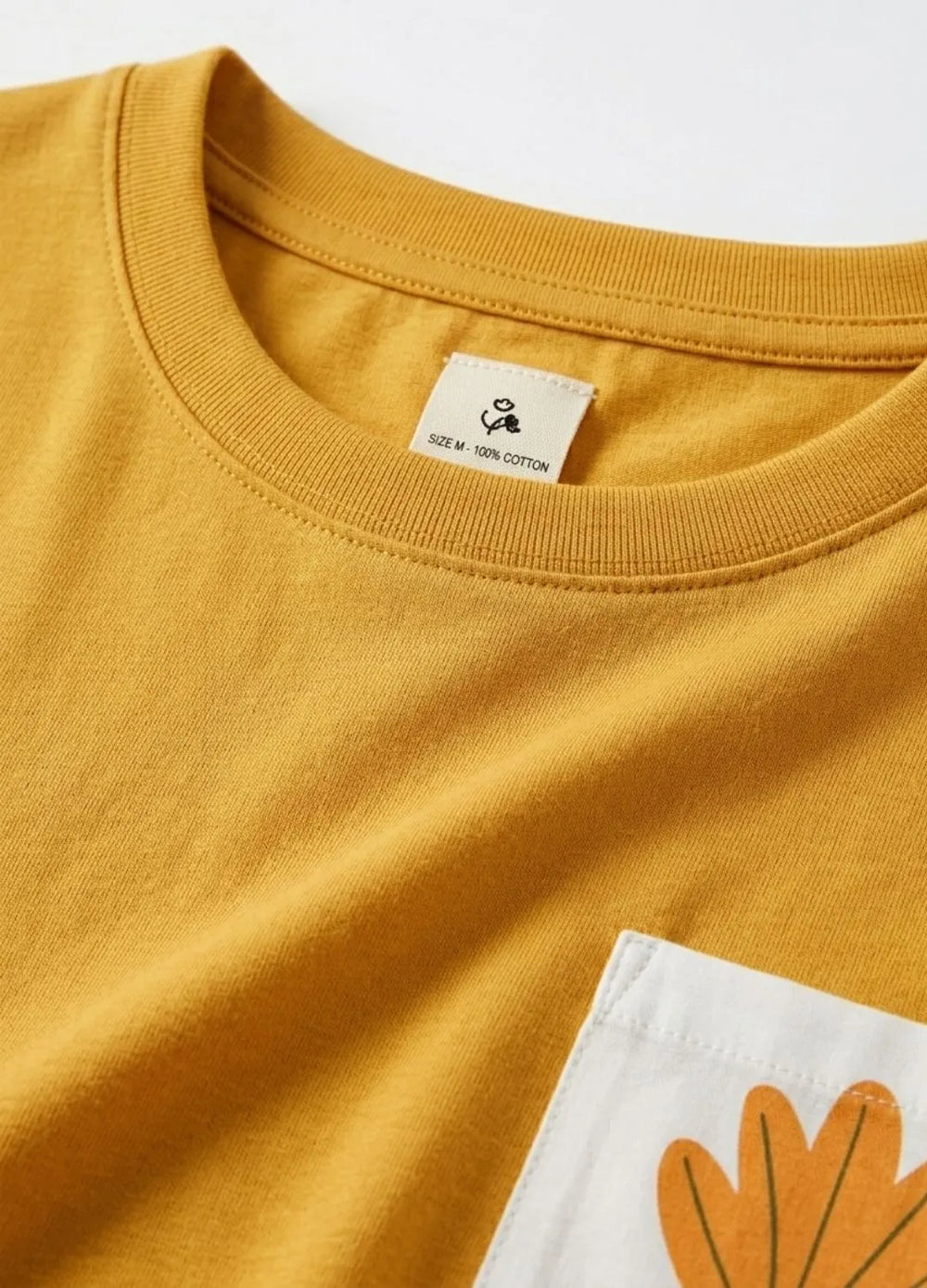 Close-up of a mustard yellow t-shirt with a white pocket featuring orange floral designs on a plain background.