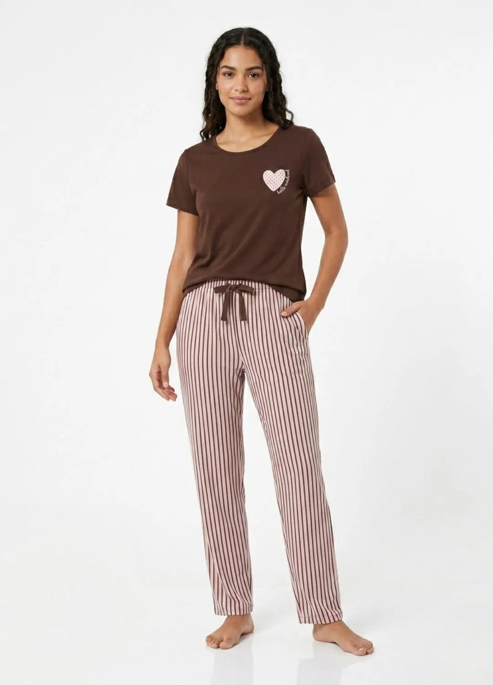 Woman wearing a brown t-shirt with a heart design and striped pajama pants on a white background