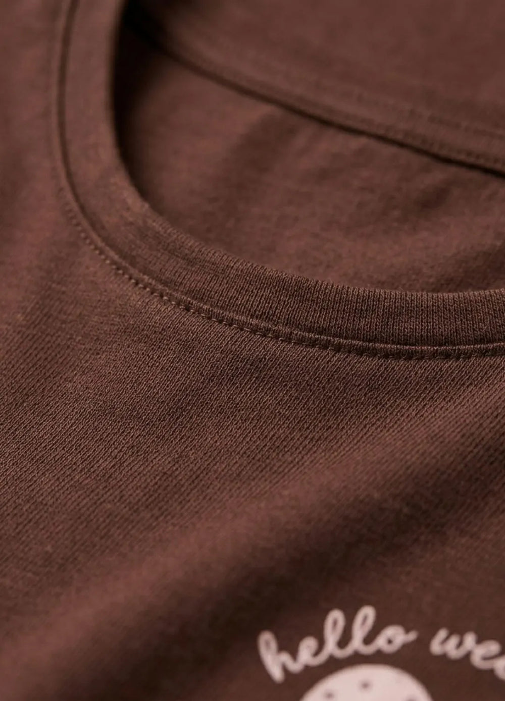 Close-up of a brown shirt with 'hello weekend' text on a white background