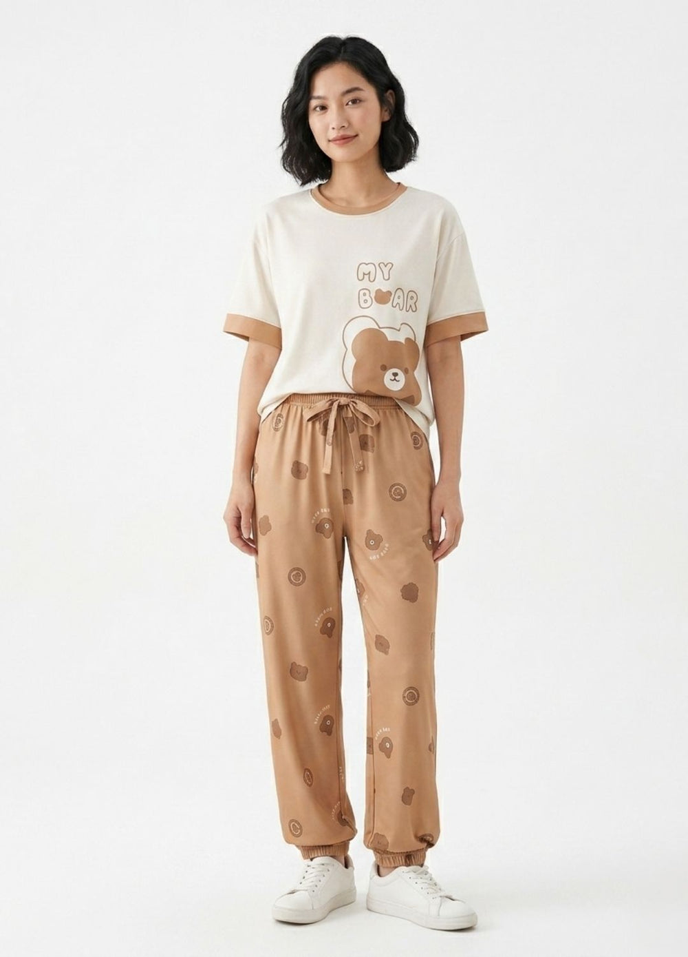 Woman wearing a cream t-shirt with a bear design and beige pants with bear prints on a white background