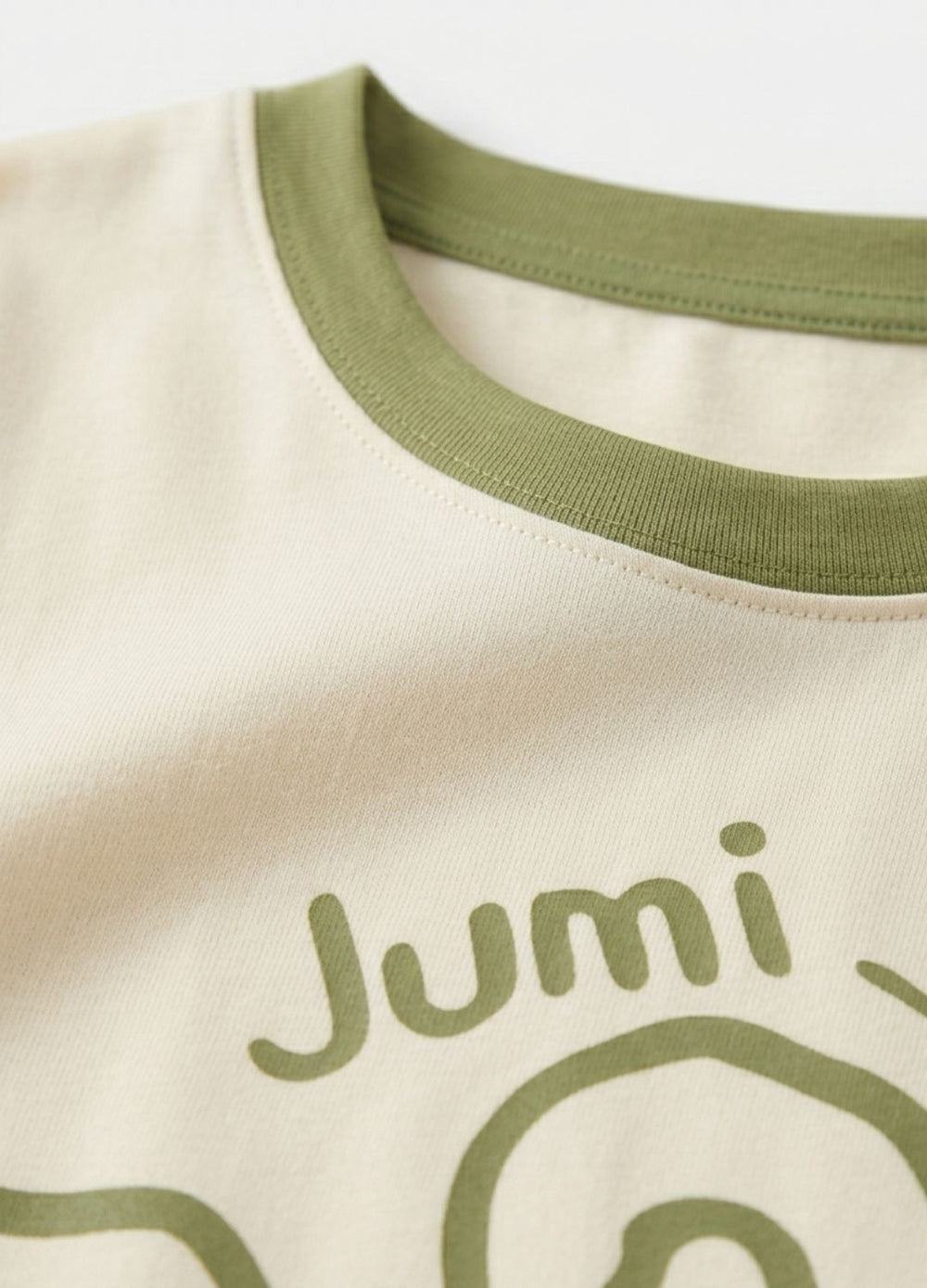 Close-up of a shirt with 'Jumi' logo on a light background